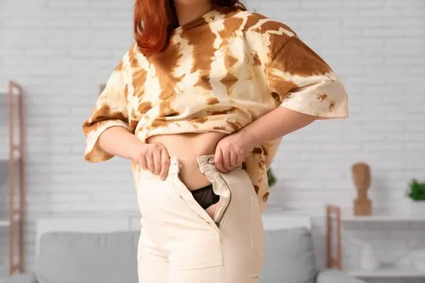 Image of woman trying to do her trousers up after pregnancy weight gain Hampshire