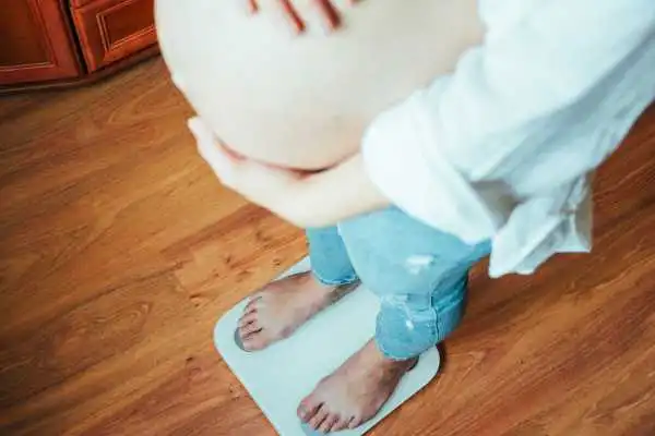 Image of woman weighing herself and experiencing weight gain through pregnancy Hampshire